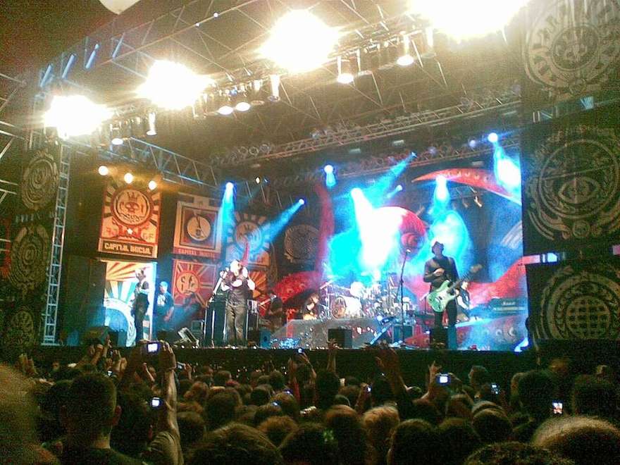 Capital Inicial ao vivo em palco de grande porte, com os banners da banda ao fundo