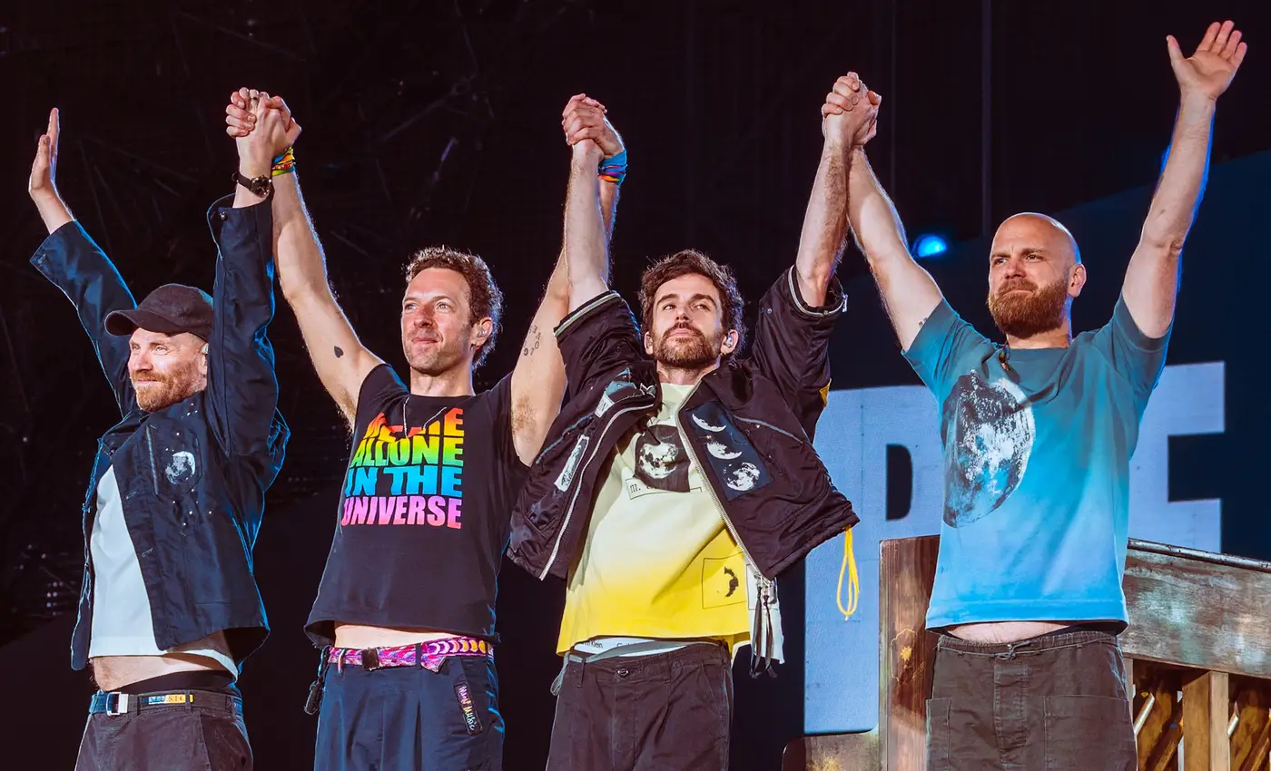 Os quatro integrantes do Coldplay de mãos dadas e braços erguidos no palco de Wembley