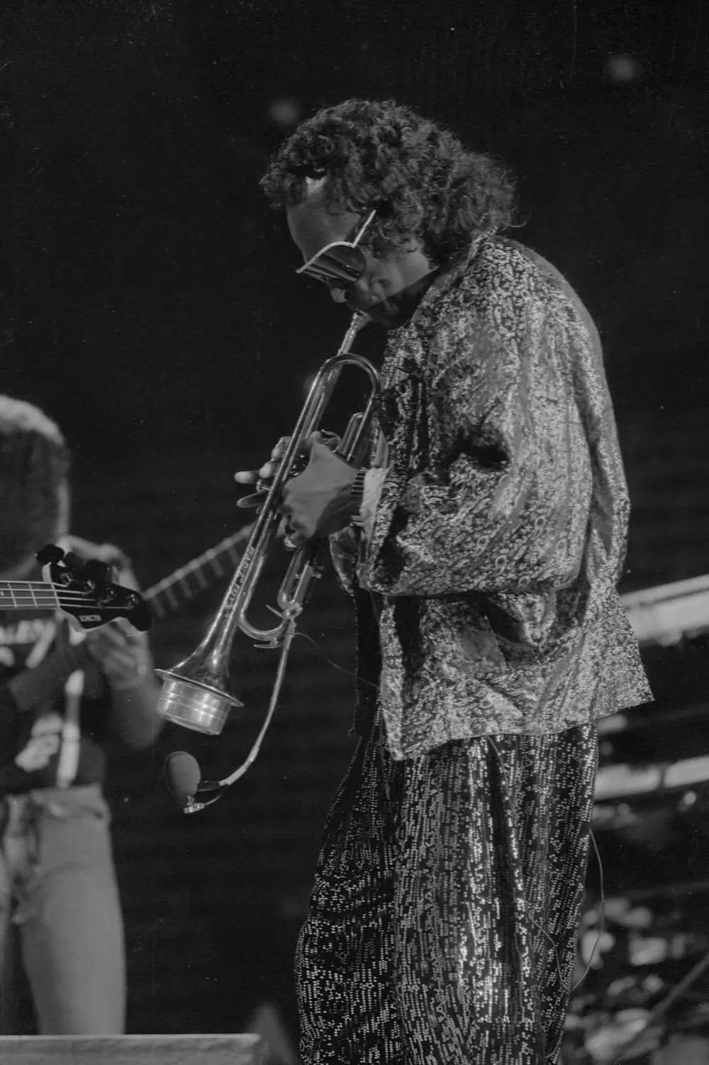 Miles Davis tocando trompete ao vivo em 1987, de óculos escuros e paletó estampado